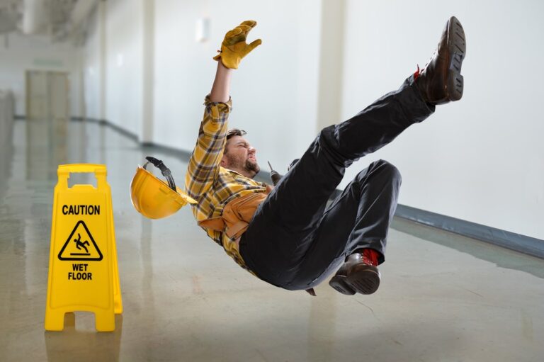Worker slipping and falling on a wet floor in a workplace environment, with a caution sign visible nearby.
