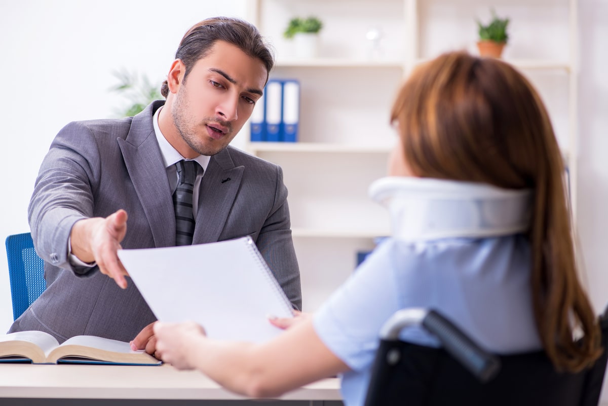 Male personal injury lawyer discussing case documents with an injured client wearing a neck brace in an office setting.