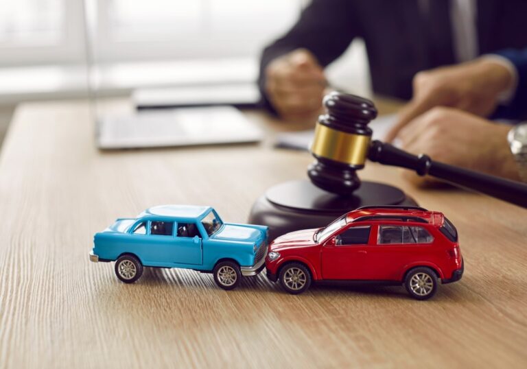 Two toy cars in a collision with a gavel on a desk, symbolizing car accident legal proceedings.