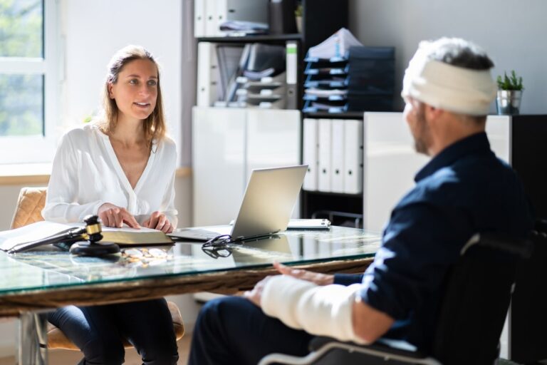 Lawyer consulting with an injured man wearing a head bandage and arm cast in an office.