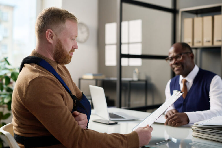 A man with an arm injury consulting a car accident lawyer in an office.