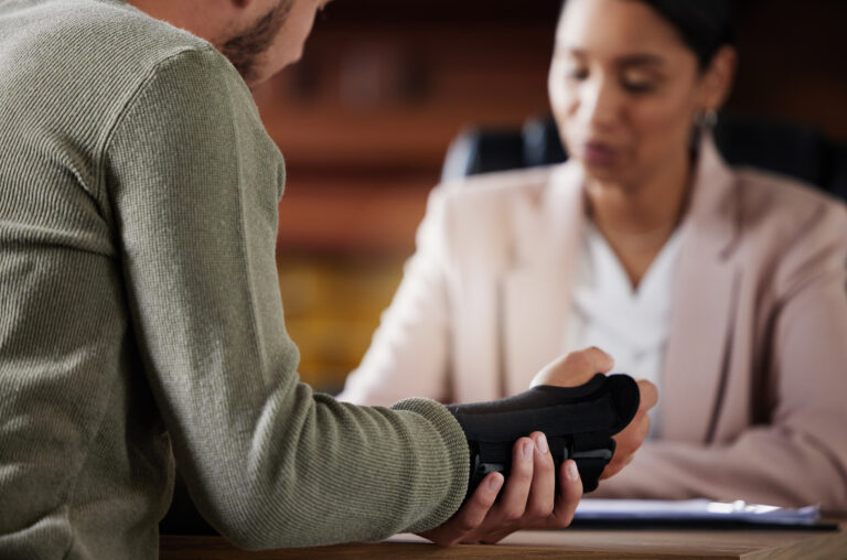 Close-up of a man with an arm brace discussing with a woman in a professional setting.