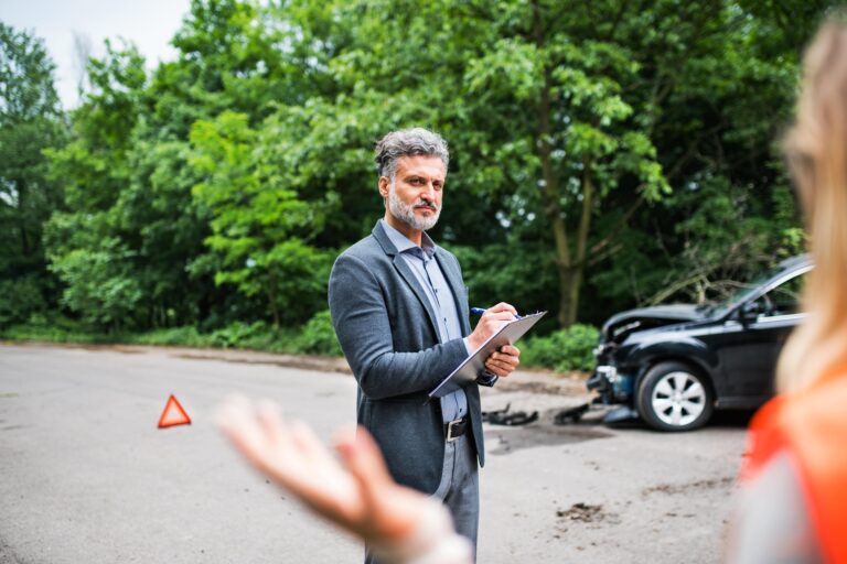 An insurance adjuster taking notes at the scene of a truck accident with damaged vehicles in the background.