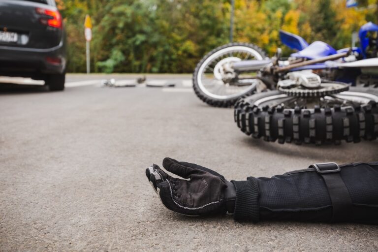 Motorcycle accident scene with a fallen bike and injured rider's hand on the road, highlighting the importance of expert legal representation.