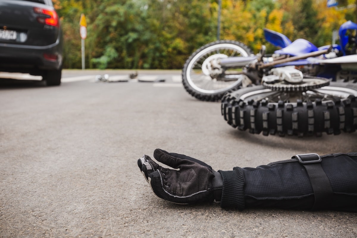 Motorcycle accident scene with a fallen bike and injured rider's hand on the road, highlighting the importance of expert legal representation.