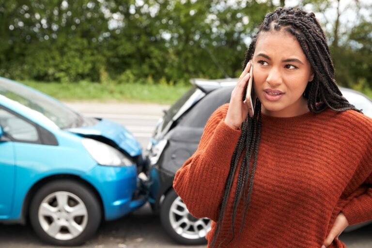 Concerned woman making a phone call after a car accident involving a blue and black car.