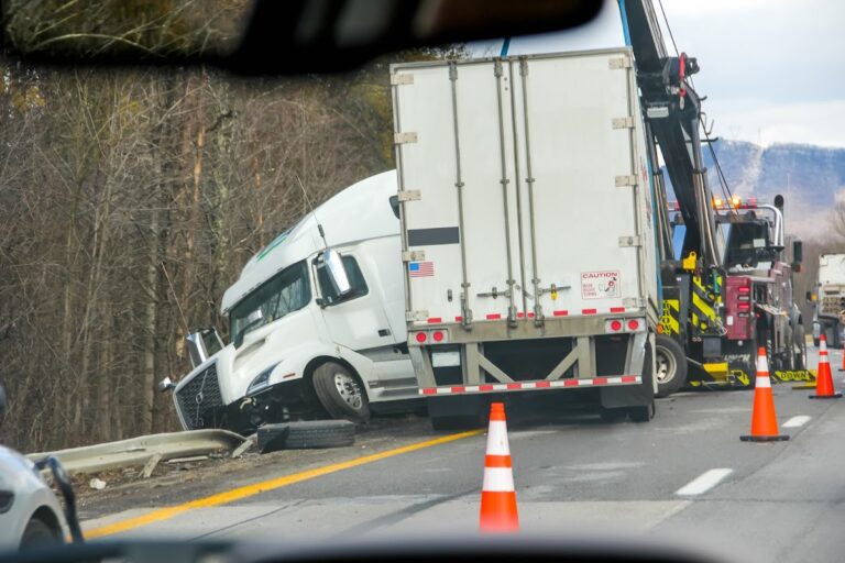 A semi-truck involved in an accident being towed from the highway, with orange traffic cones marking the scene.